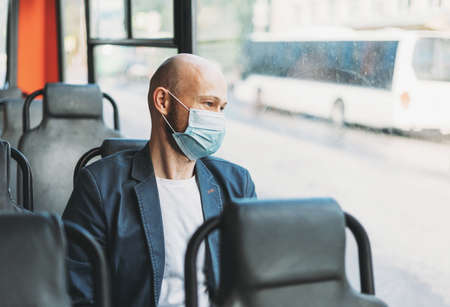 Adult bald bearded man in medical face mask looking out window in bus. New normal, concept of...