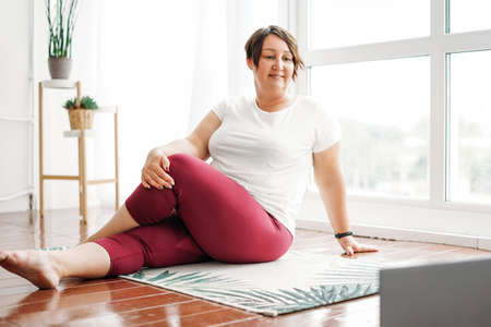 Adult charming brunette woman in glasses plus size body positive working with laptop at home