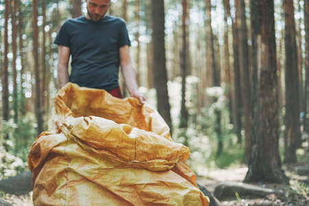 Adult man volunteer cleans forest of garbage in large bag. Volonteer picking up trash in woods