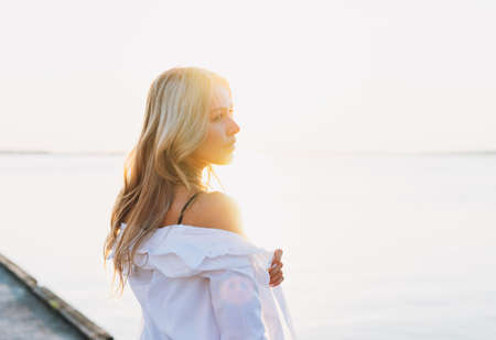 Close up portrait of beautiful blonde young woman in white shirt and straw hat on sunset