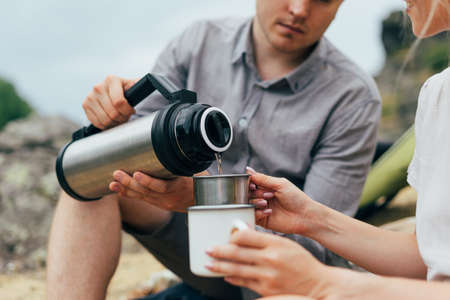 Young couple travelers in the casual outfits with tent. Man pours tea  . Local tourism, weekend tripの写真素材