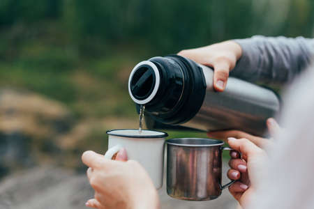 Young couple travelers in casual outfits with tent. Man pours tea from . Local tourism, weekend tripの写真素材