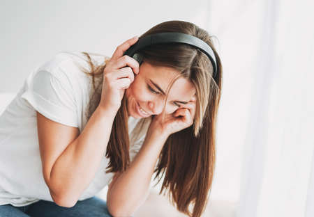 Portrait of smiling young woman brown hair and green eyes with freckles in white t-shirt and jeans listening music by headphonesの写真素材