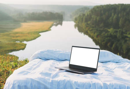 Open laptop with white screen on bed in nature against beautiful landscape early morning, mock upの写真素材