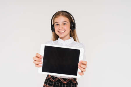 Cute smiling teen girl in school uniform with headphones and tablet in her hands isolated on white background, mockupの写真素材