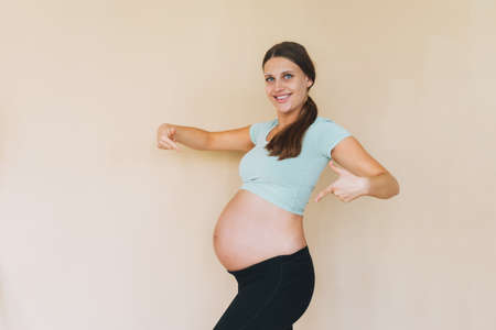Young smiling pregnant woman in sportswear isolated on beige background