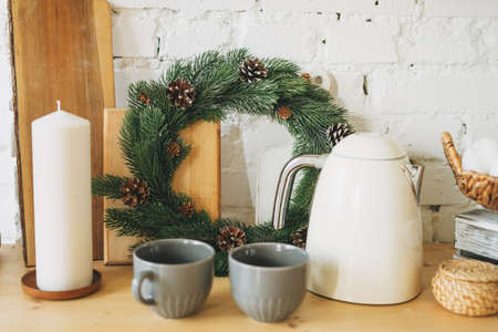 Candle, christmas wreath of fir branches, teapot and cups on kitchen, cozy home, scandinavian design