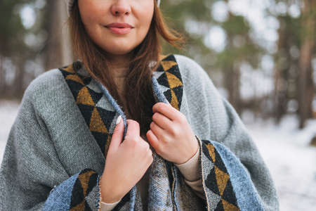 Young brunette beautiful woman in hat and gray poncho in the winter forest