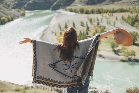 Brunette young woman traveler in poncho near mountain river, country side