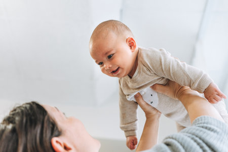 Cute baby feet in beige socks, child with mother on the bed, happy motherhood