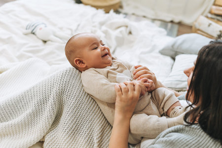 Young mother having fun with cute baby boy on bed, natural tones, love emotionの写真素材