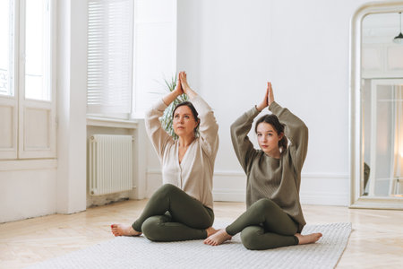 Attractive mother middle age woman and daughter teenager ptactice yoga together in the bright roomの写真素材