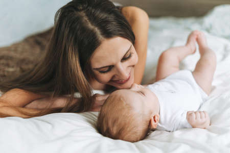 Young mother having fun with cute baby girl on bed, natural tones, selective focus