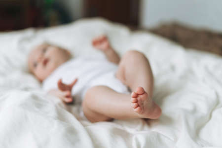 Cute baby girl 2-4 month on bed with white linen, natural tones, selective focusの写真素材