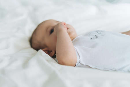 Cute baby girl 2-4 month on bed with white linen, natural tones, selective focusの写真素材
