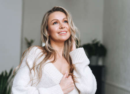 Blonde sensual young woman with long hair in underwear and white shirt on window sill at bright...