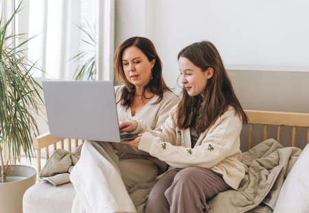 Mother middle aged woman and daughter teenager using laptop together in light interior