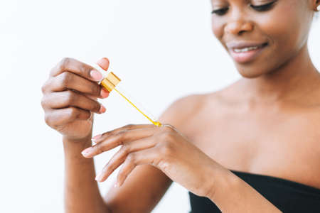 Beauty portrait of smiling african young woman in underwear with cosmetic oil for hands and body on...