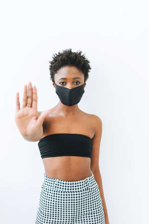 Beautiful young African American woman in black top and face mask isolated on the white background, stop coronavirus conceptの写真素材