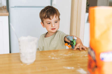 Toddler boy have fun while cooking with flour at the table in kitchen at home. Boy playing with toyの写真素材