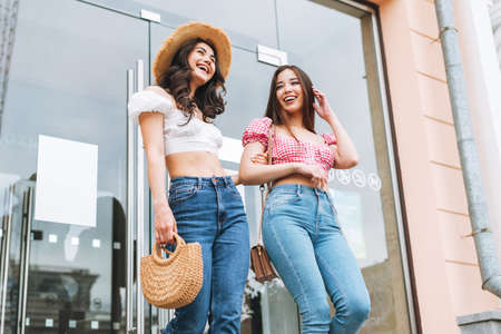 Happy smiling beautiful brunette young women friends in summer clothes with juice in hands sitting...