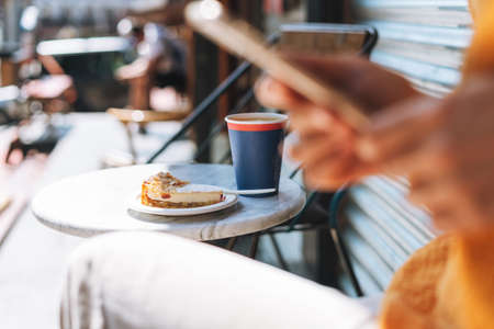 Young woman with long blonde hair wearing sunglasses and yellow longsleeve with mobile phone in her hands in cafeの写真素材
