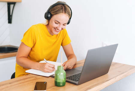 Young smiling blonde woman freelancer in yellow headphones working on laptop on the table at cafe