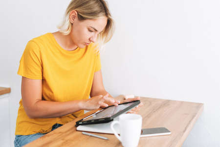 Young blonde woman in yellow t-shirt studies cryptocurrency charts and stock quotes on digital...