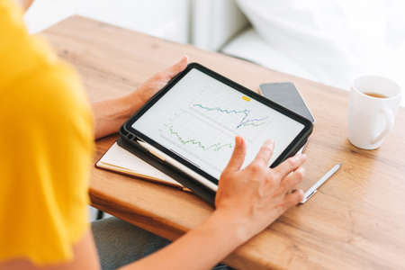 Young blonde woman in yellow t-shirt studies cryptocurrency charts and stock quotes on digital...