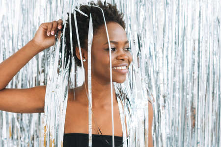 Portrait of happy dancing young African American woman in black top on the sparkly silver...