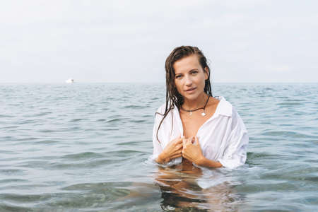 Fashion beauty portrait of young beautiful woman with long hair and white shirt in sea. Unity with...
