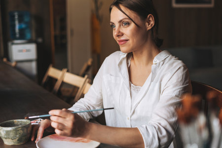 Young pretty woman in cozy gray scarf with mug of tea in hands looks out the window and rests in studioの写真素材