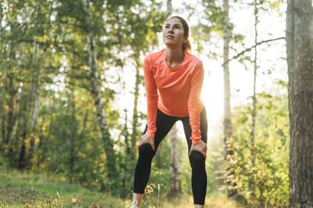 Young slim woman brunette in sport clothes running at the forest on golden hour sunrise time. Health and wellness, fitness lifestyleの写真素材
