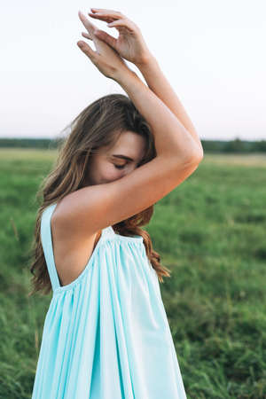 Young beautiful carefree long hair woman in light blue turquois dress in sunset field. Sensitivity to nature concept, feminityの写真素材