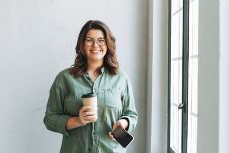 Young smiling brunette woman nutritionist plus size in white shirt working at laptop on table with...