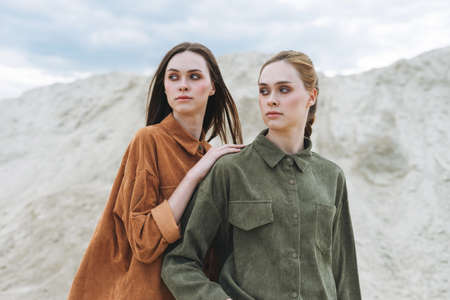 Fashion beauty portrait of young women sisters in brown organic velvet jeans shirts on the desert backgroundの写真素材