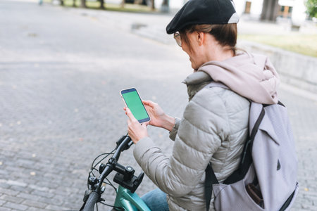 Young smiling brunette woman in casual clothes using social media on mobile phone sitting at green cafeの写真素材