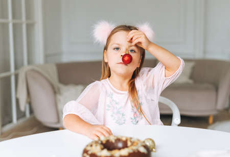 Funny cute little girl with long hair in light pink dress with red christmas ball in hands in the bright living room at home. Christmas time, birthday girlの写真素材