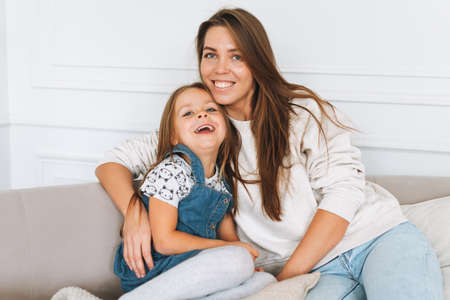 Portrait of Young happy family on sofa in bright living room. Happy woman with cute little girl smile and look at the camera. Joint leisure at homeの写真素材