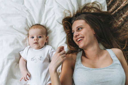 Young woman mom with long hair holding baby girl on hands near window at the home