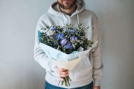 Young man in gray hoodie with bouqet of flowers in hands on the gray background