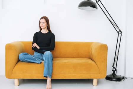 Young unhappy woman teenager girl with long hair in jeans sitting on floor in closed position by the door at home, negative emotionの写真素材