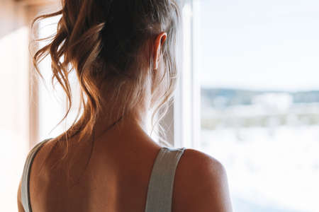 Close up photo of Young slender fitness blonde woman from back near the window of home