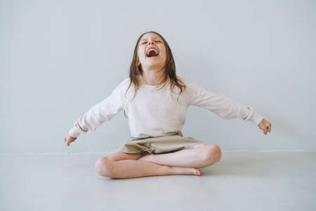 Screaming emotional little girl with long hair in natural tones clothes at light studio