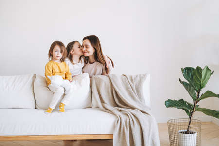 Young happy family with one parent woman mother with two children girls on couch in living room at...