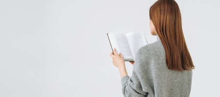 Beautiful young woman with dark long hair in gray knitted sweater reading book, banner on white...