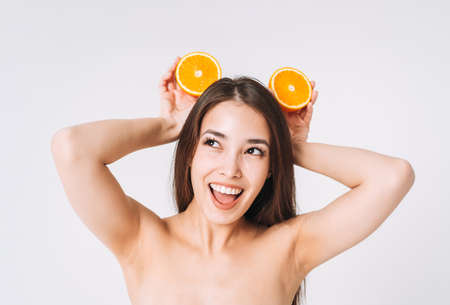 Portrait of happy young beautiful asian woman with dark long hair in jeans sitting on white background isolatedの写真素材