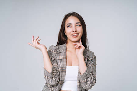 Young unhappy asian business woman with long hair in suit and jeans holding her hands on head on gray backgroundの写真素材