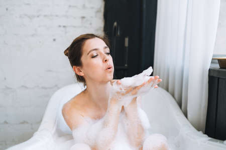 Young happy woman taking bath with foam at home, treat yourself