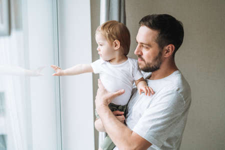 Happy father young man and baby girl little daughter having fun reading a book in children room at homeの写真素材